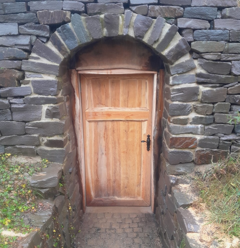 Erdkeller-Eingang, aus Grauwacke-Natursteinen gemauert, mit Türe aus Robinien-Holz